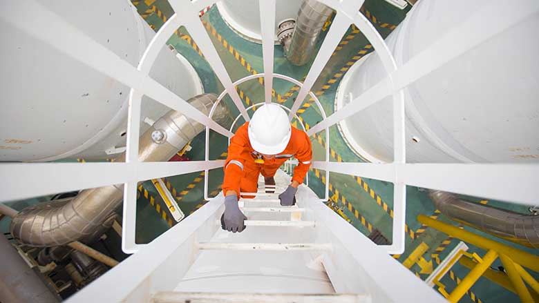 مهندس يتسلق سلمًا في منشأة لمعالجة النفط والغاز. © مصور النفط والغاز / Shutterstock